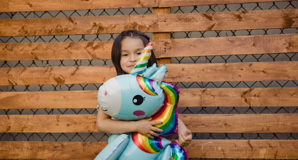 a girl standing with a toy in front of a pallet fence